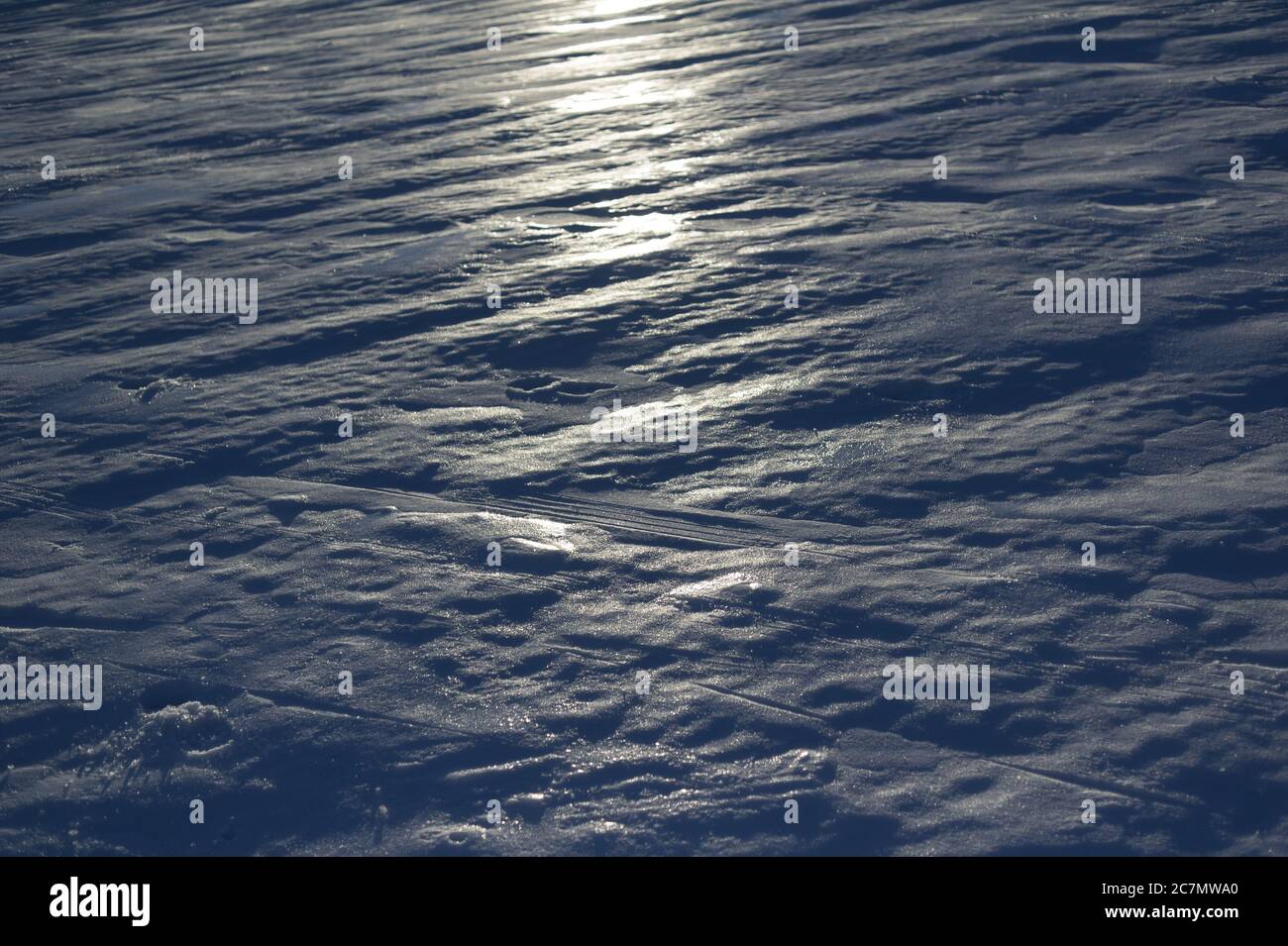 Detail of ice and snow with tracks and imprints. . Light of sun is reflecting on the surface. Backlight underexposure Stock Photo