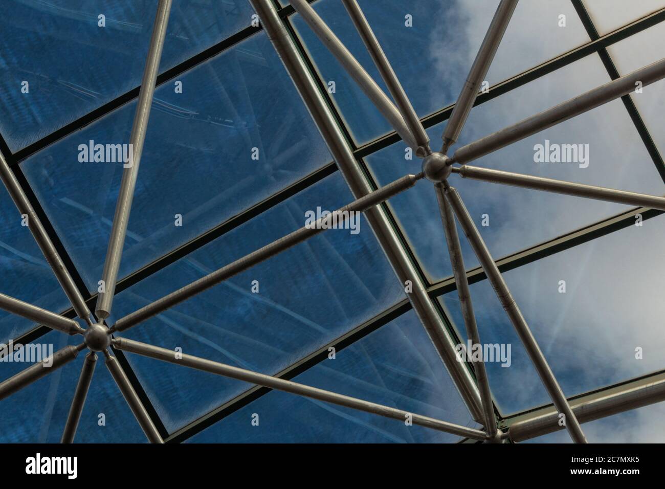 Elaborate steel metal greenhouse structure with diffuse view of deep blue sky with clouds, horizontal aspect Stock Photo