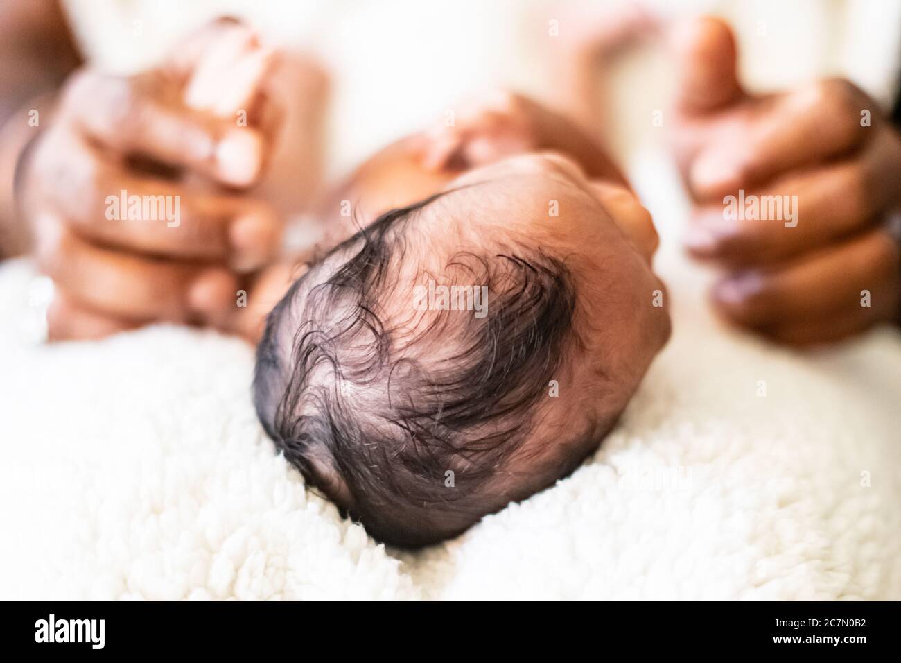 View of African American baby infant girl with focus on the top of her head while father holds her hands in his. Stock Photo