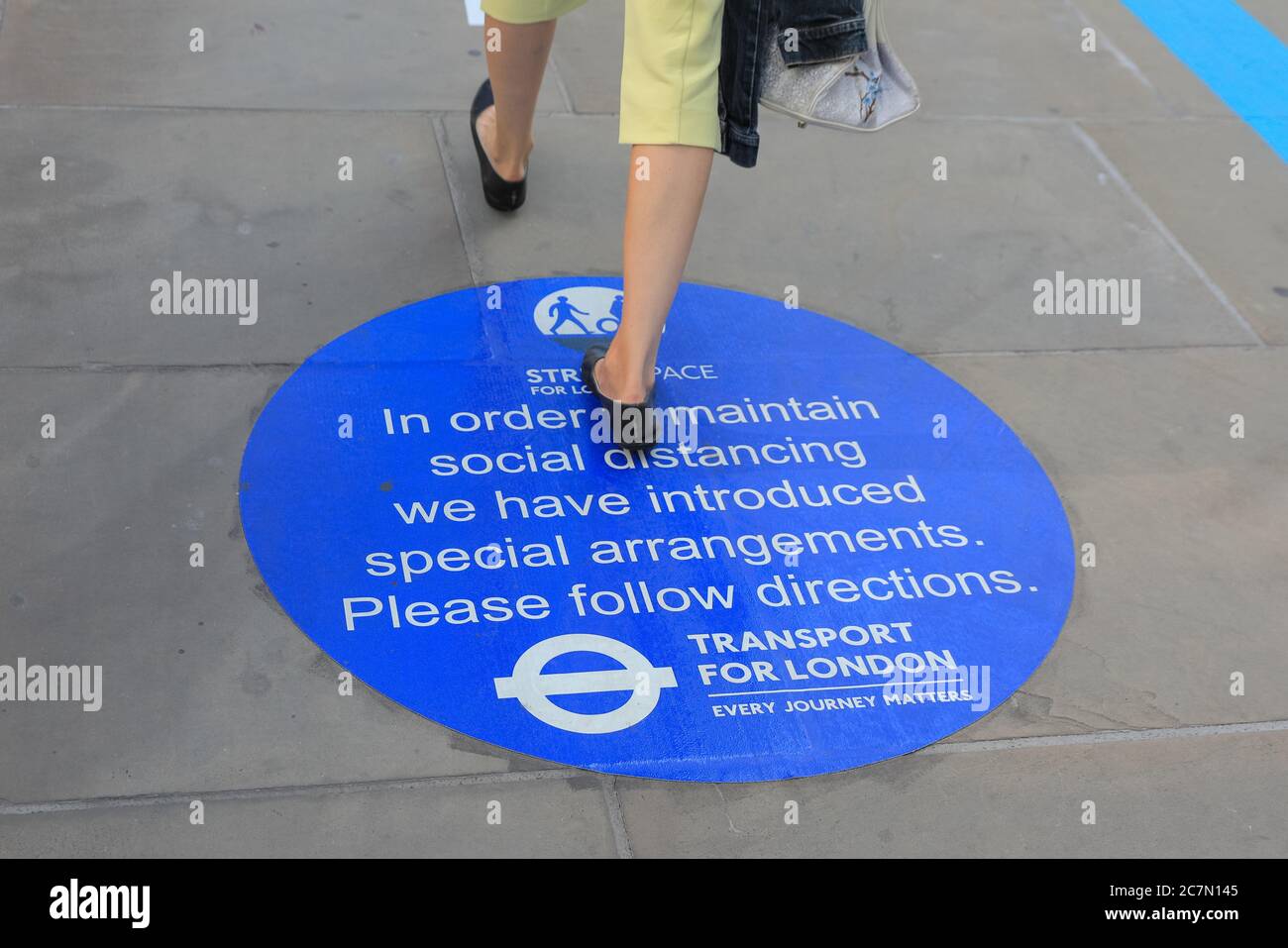 London, UK. 18th July, 2020. A woman walks across a sign on London Bridge reminding people of social distancing rules. Central London appeared to get busier today with more people leaving their homes to enjoy the sunny weather. Social distancing rules appeared to be adhered to in most places, but some areas are already getting crowded. Credit: Imageplotter/Alamy Live News Stock Photo