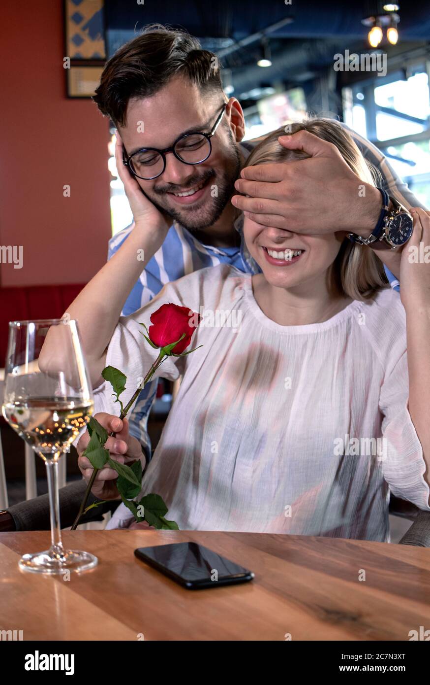 Young romantic couple in a fancy restaurant. Boyfriend surprise his  girlfriend with a red rose behind her back Stock Photo - Alamy