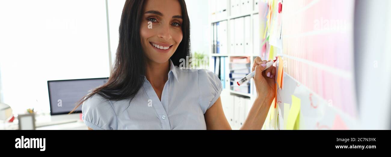 Beautiful smiling brunette caucasian woman writing something on whiteboard Stock Photo