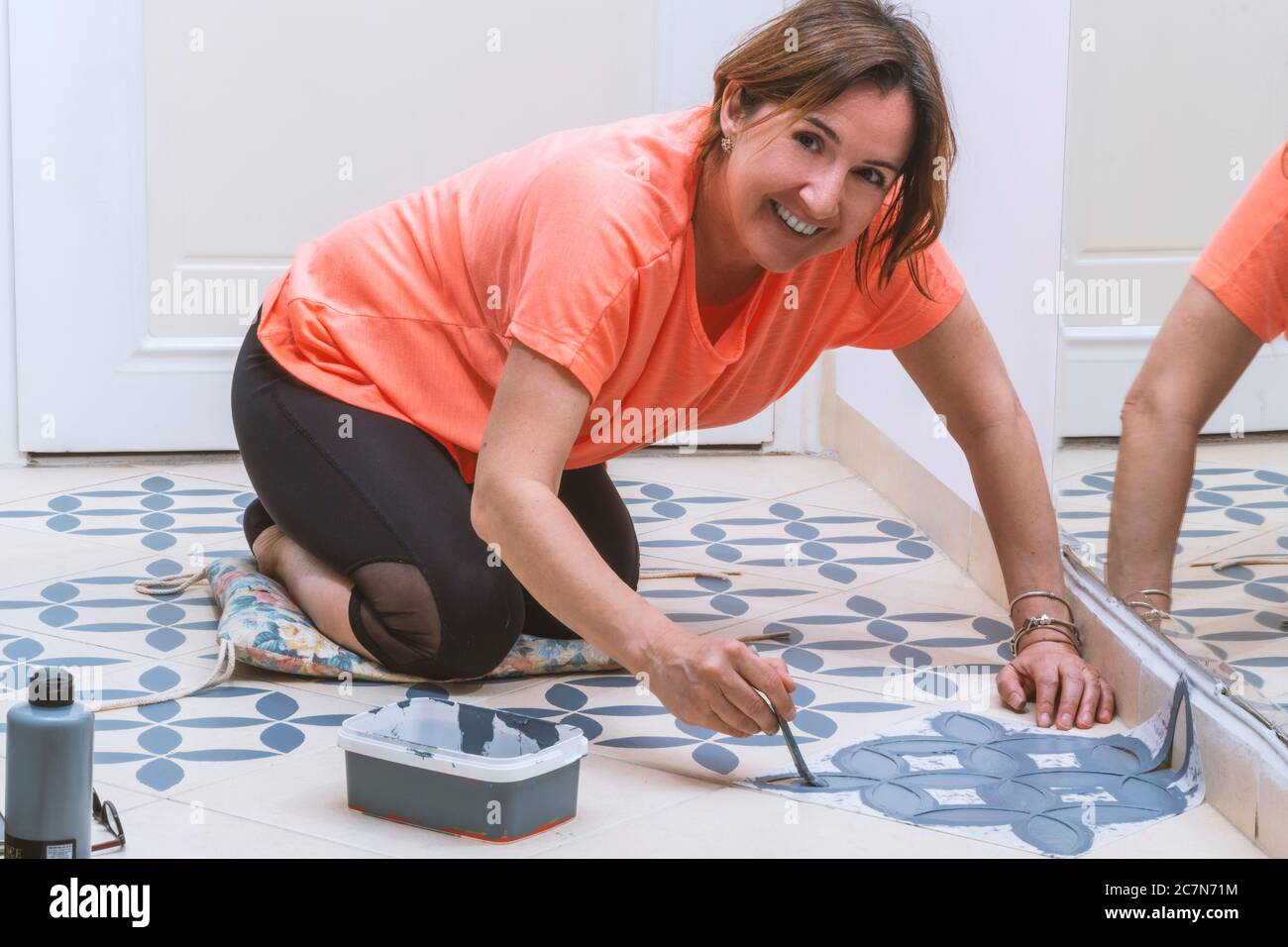 Stay at home and home improvement concept: Young caucasian woman with orange T- shirt is painting tiles of her home. Stock Photo