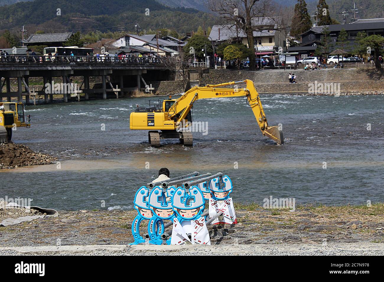 Construction side at Kamo river, Kyoto with cute comic construction barriers and beyond an excavator in the river and people walking over bridge. Stock Photo