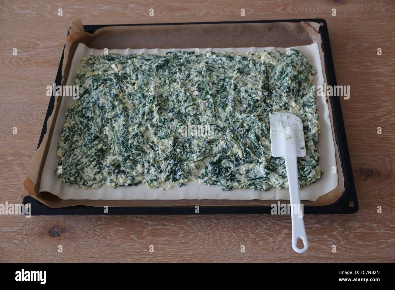 Preparation of a spinach paste. The puff dough spread on a sheet and covered with ricotta spinach filling seasoned with salt, pepper and garlic. Stock Photo