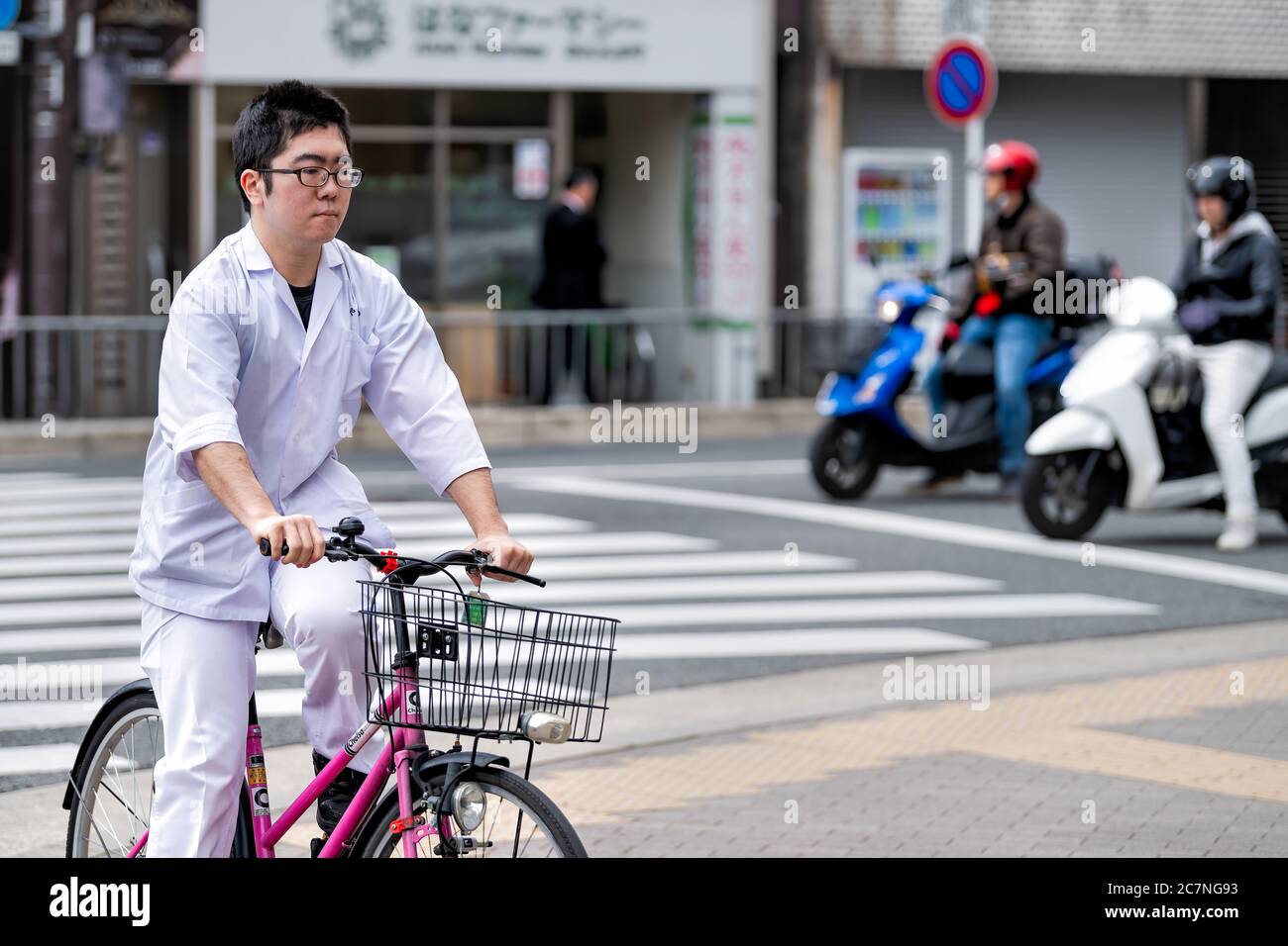 Kyoto, Japan - April 17, 2019: Japanese person on bicycle riding bike basket on street candid city life road in white uniform Stock Photo
