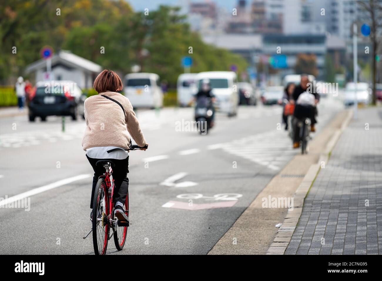 Kyoto, Japan - April 17, 2019: Japanese person back on bicycle riding bike on street candid city life with traffic cars road near station Stock Photo