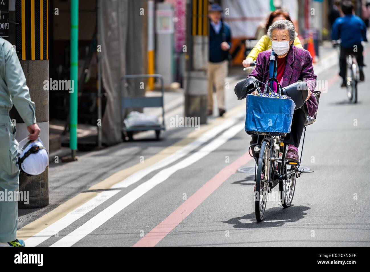 Kyoto, Japan - April 17, 2019: Kyoto downtown district with people local Japanese senior elderly person wearing mask face covering riding bicycle bike Stock Photo