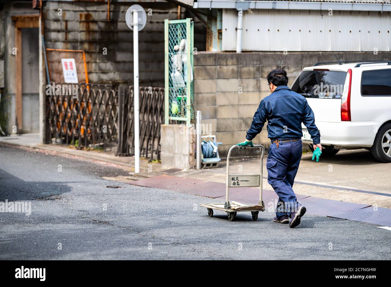 Kyoto, Japan - April 17, 2019: Japanese delivery man carrying pushing trolley walking on street candid city life of worker Stock Photo