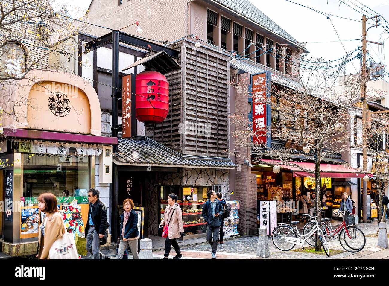 Nara, Japan - April 15, 2019: People many tourists walking on sidewalk street road in downtown city towards park with shops stores and signs Stock Photo
