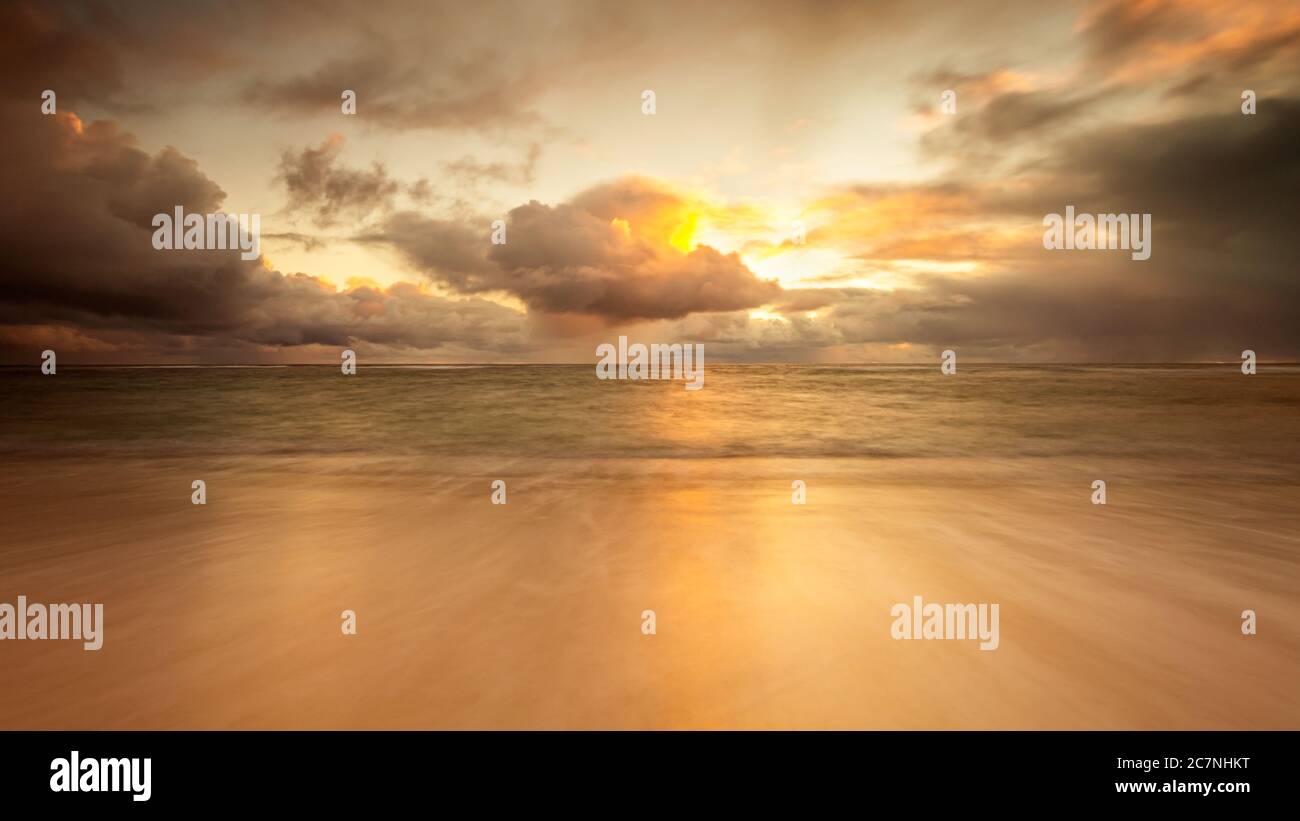 Rain cloud at the beach during sunset, with the sand lit up a golden colour Stock Photo