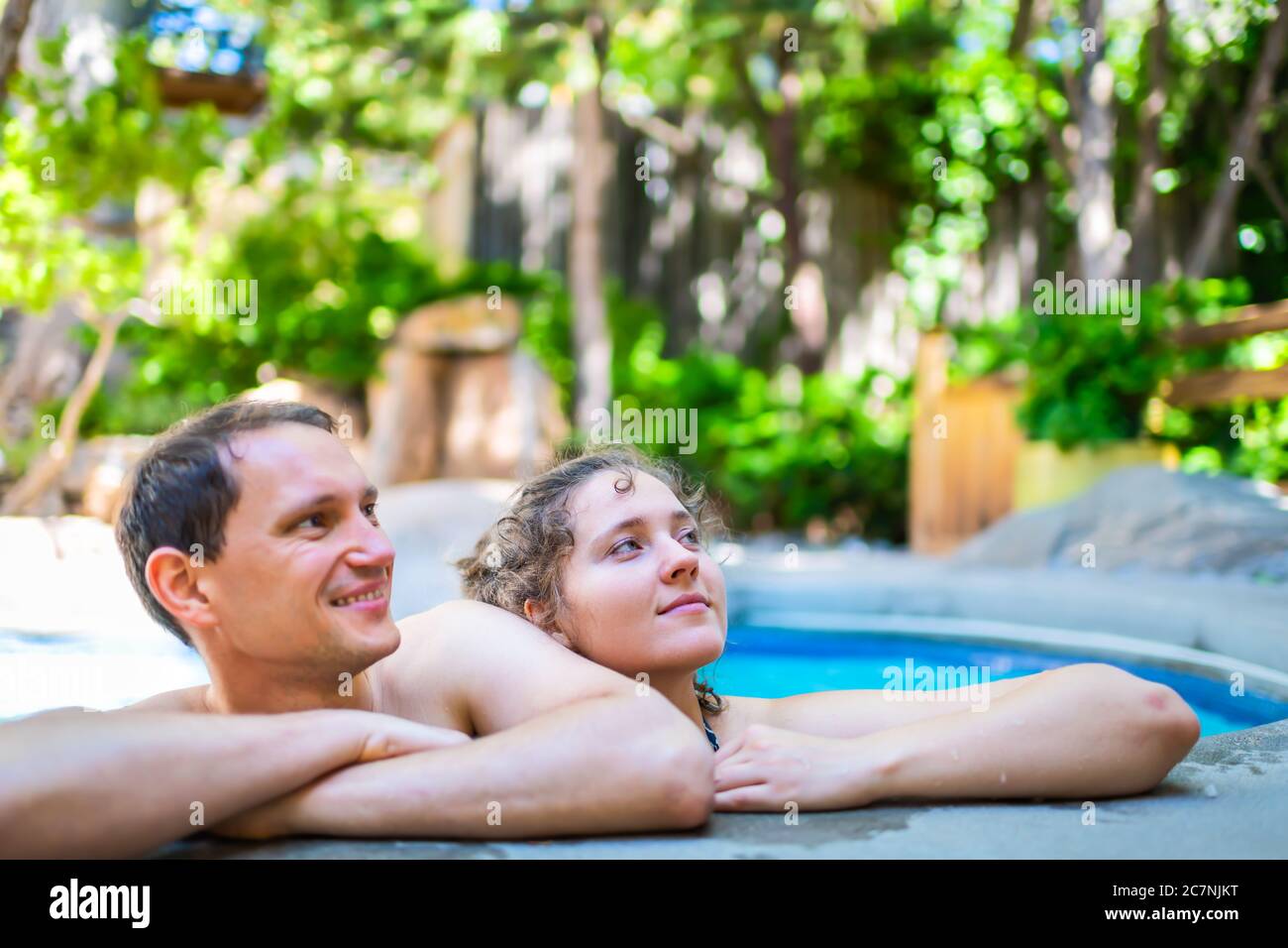 Young woman man happy romantic couple relaxing swimming leaning on stone railing edge of Japanese spa pool with colorful blue water in Japan onsen poo Stock Photo