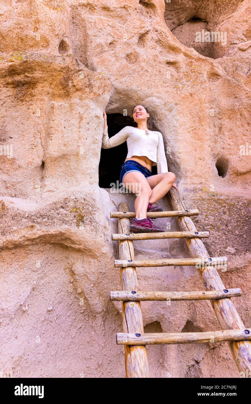 Happy woman climbing ladder on Main Loop trail in Bandelier National Monument in New Mexico during summer by canyon cliff cave Stock Photo