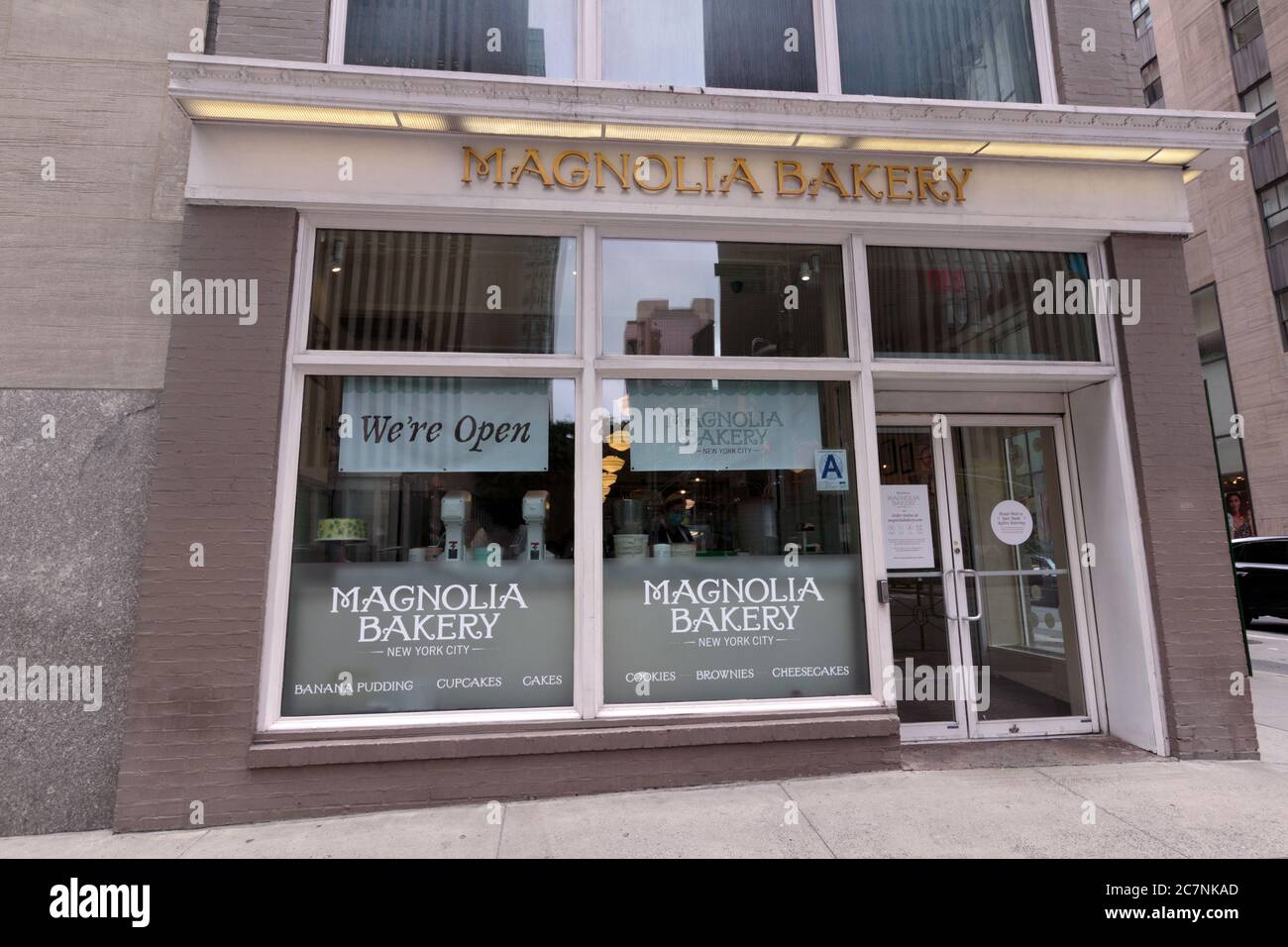storefront of the Magnolia Bakery on sixth avenue in Manhattan with a sign saying it is open during the coronavirus or covid-19 pandemic Stock Photo