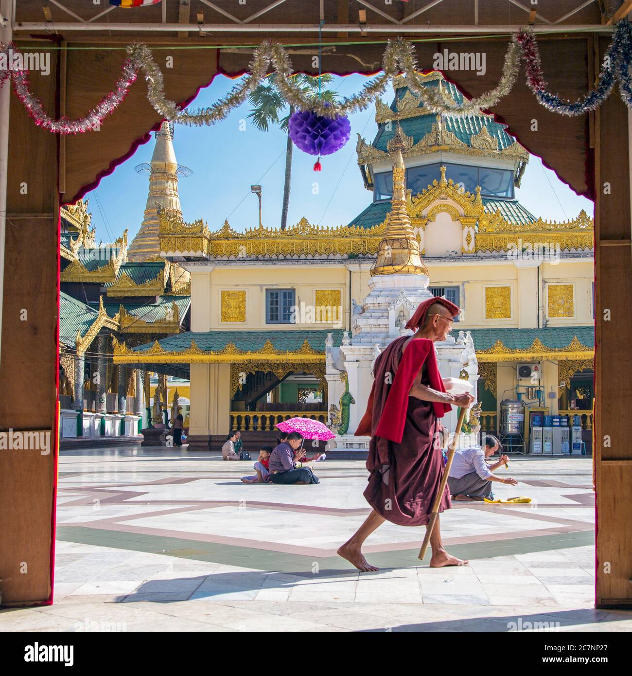 A Buddhist monk in traditional dress walks between temples at the Shwedagon Pagoda in Yangon, Myanmar Stock Photo