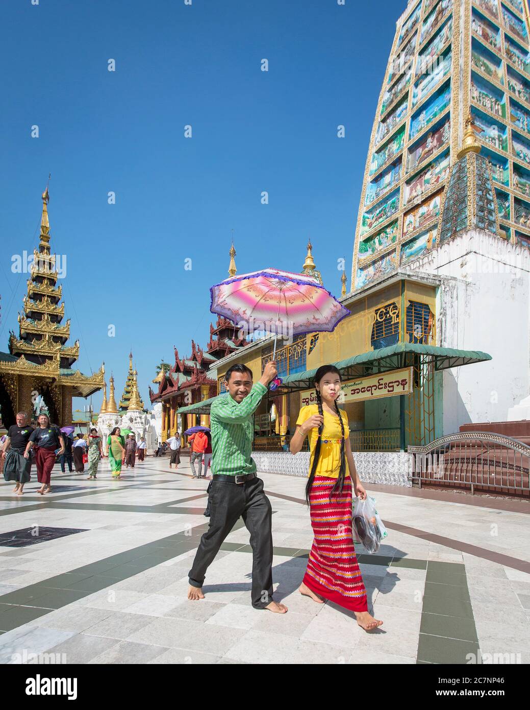 A young couple with a parasol walk between temples at the Shwedagon Pagoda in Yangon, Myanmar Stock Photo