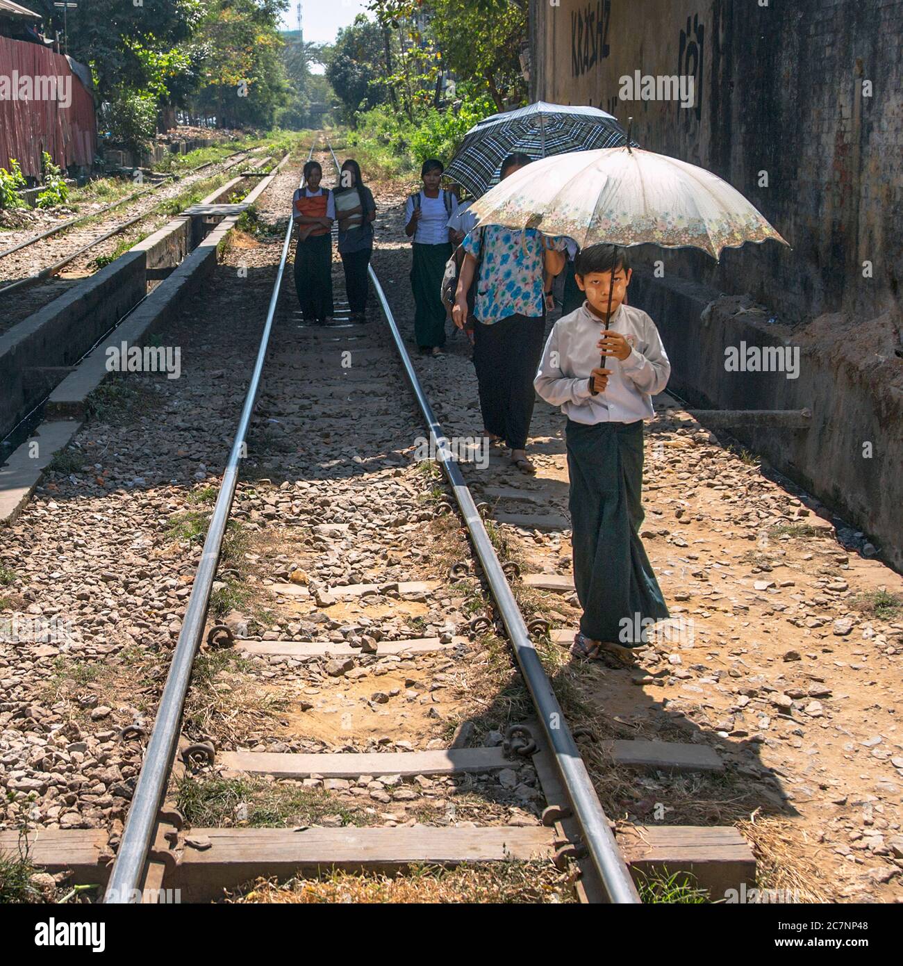 A young boy holds an umbrella as he walks along the Yangon Circular Railroad track in Yangon, Myanmar Stock Photo