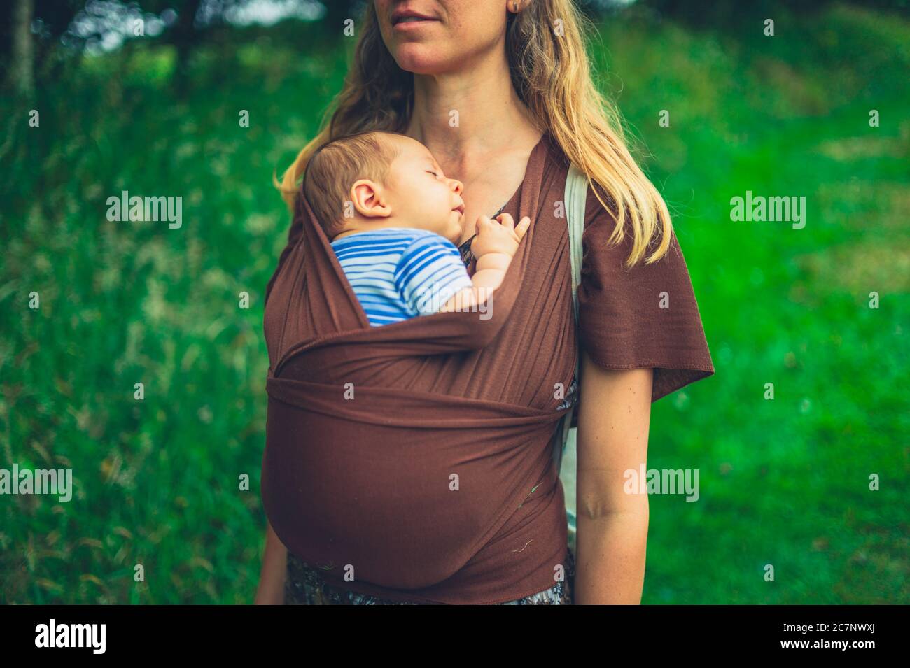 A young mother with her baby in a sling is exploring a tropical garden