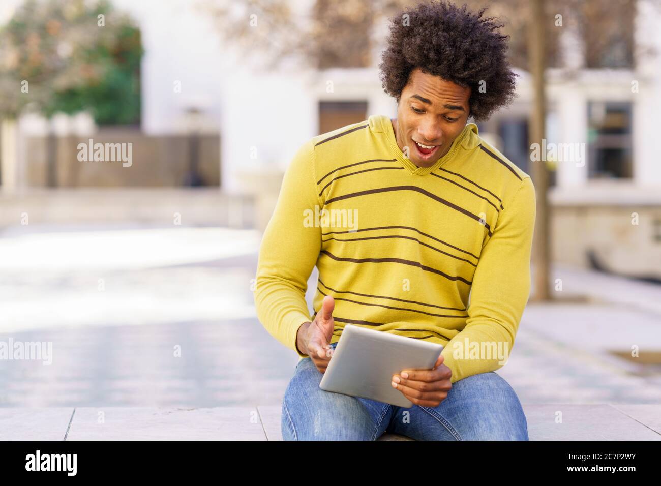 Black man using a digital tablet sitting on a bench outdoors. Stock Photo