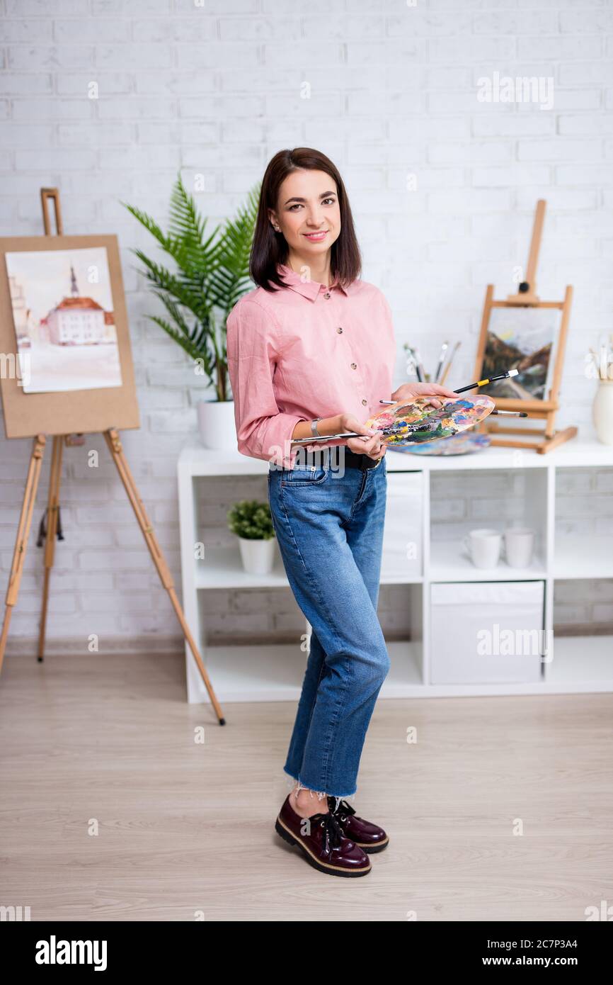 full length portrait of young woman artist posing with palette and ...