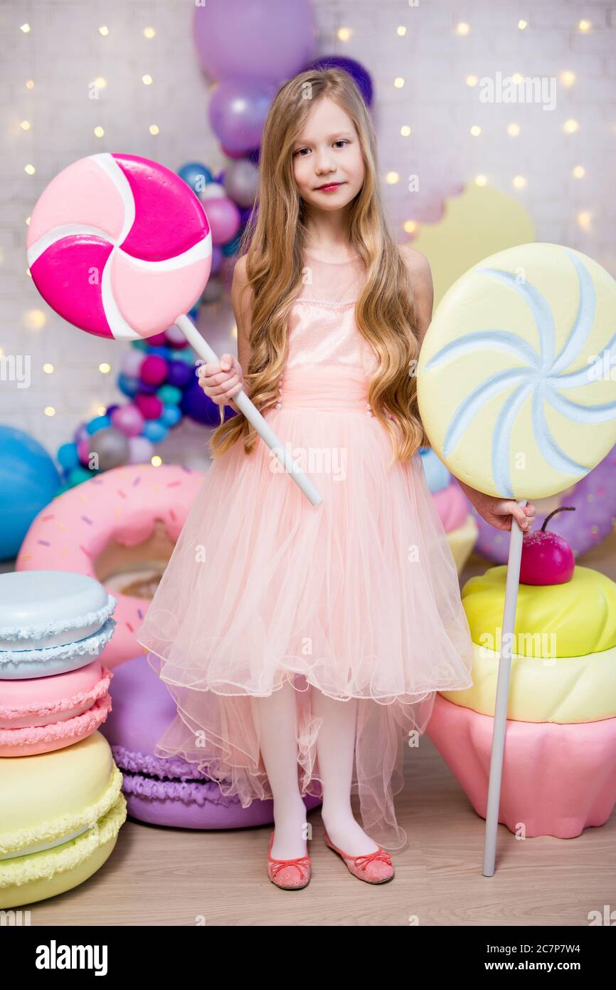 portrait of cute little girl holding huge lollipops with giant donuts and cupcakes decorations Stock Photo