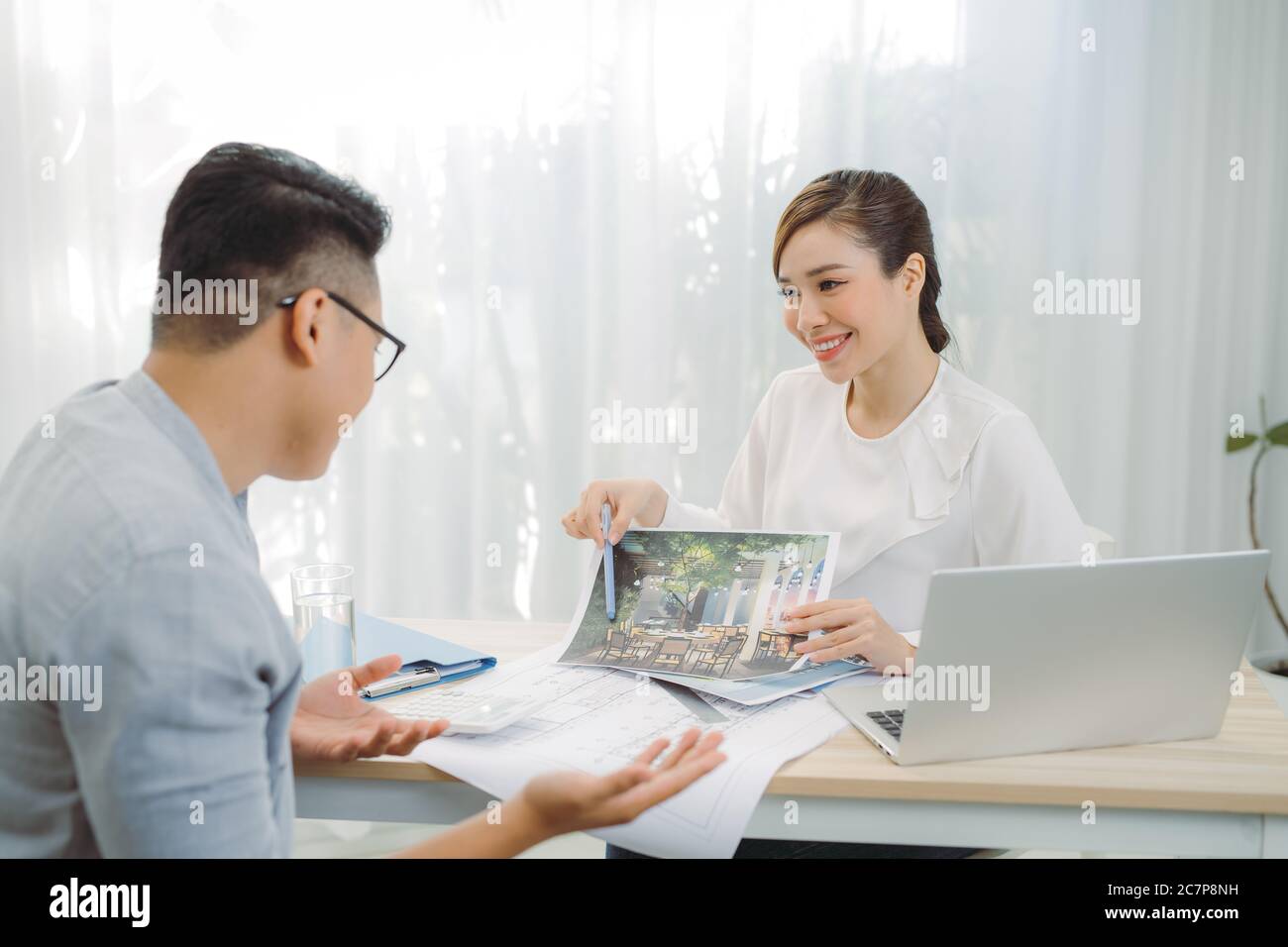 Real-estate agent showing house plans for client at office. Stock Photo