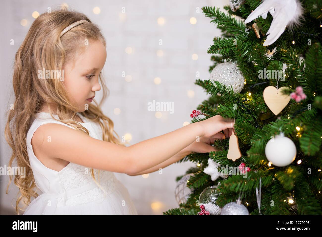 portrait of happy cute little girl decorating Christmas tree at home ...