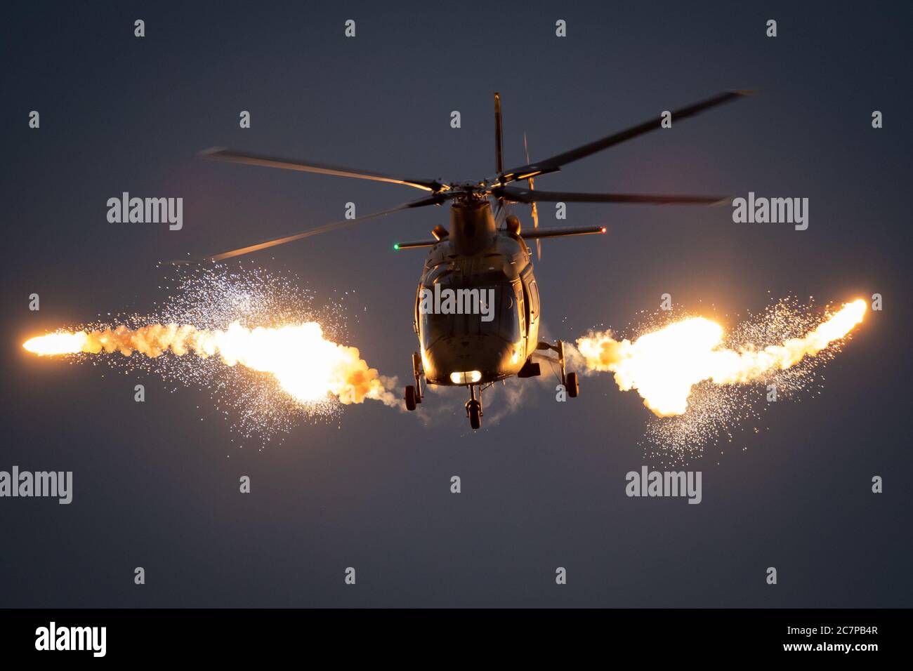 Military helicopter in flight firing off flare decoys at night. Stock Photo