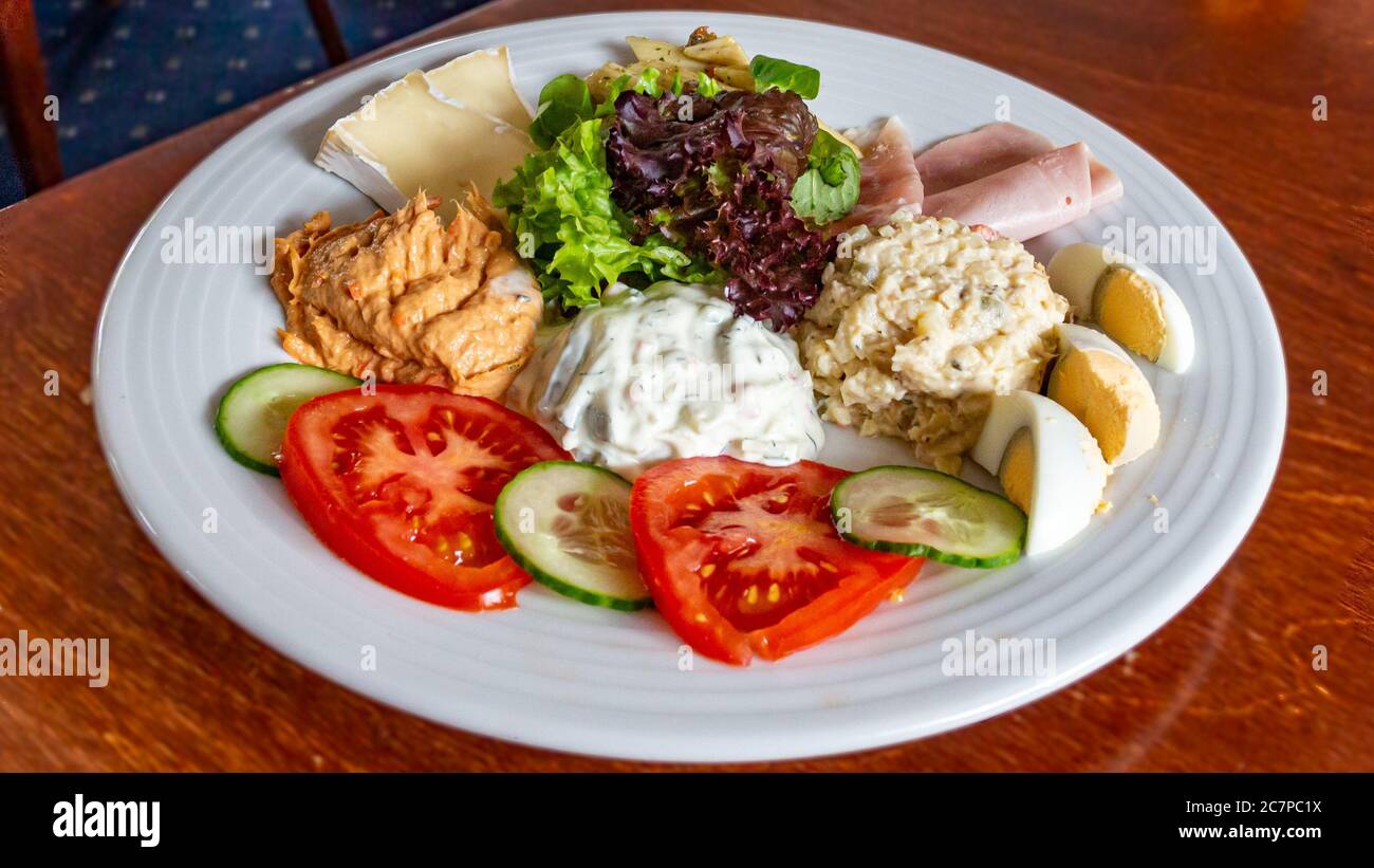 Dish with a combination of three different salads: Russian, tuna and shrimp accompanied by pasta, camembert cheese, human ham, egg pieces and lettuce Stock Photo