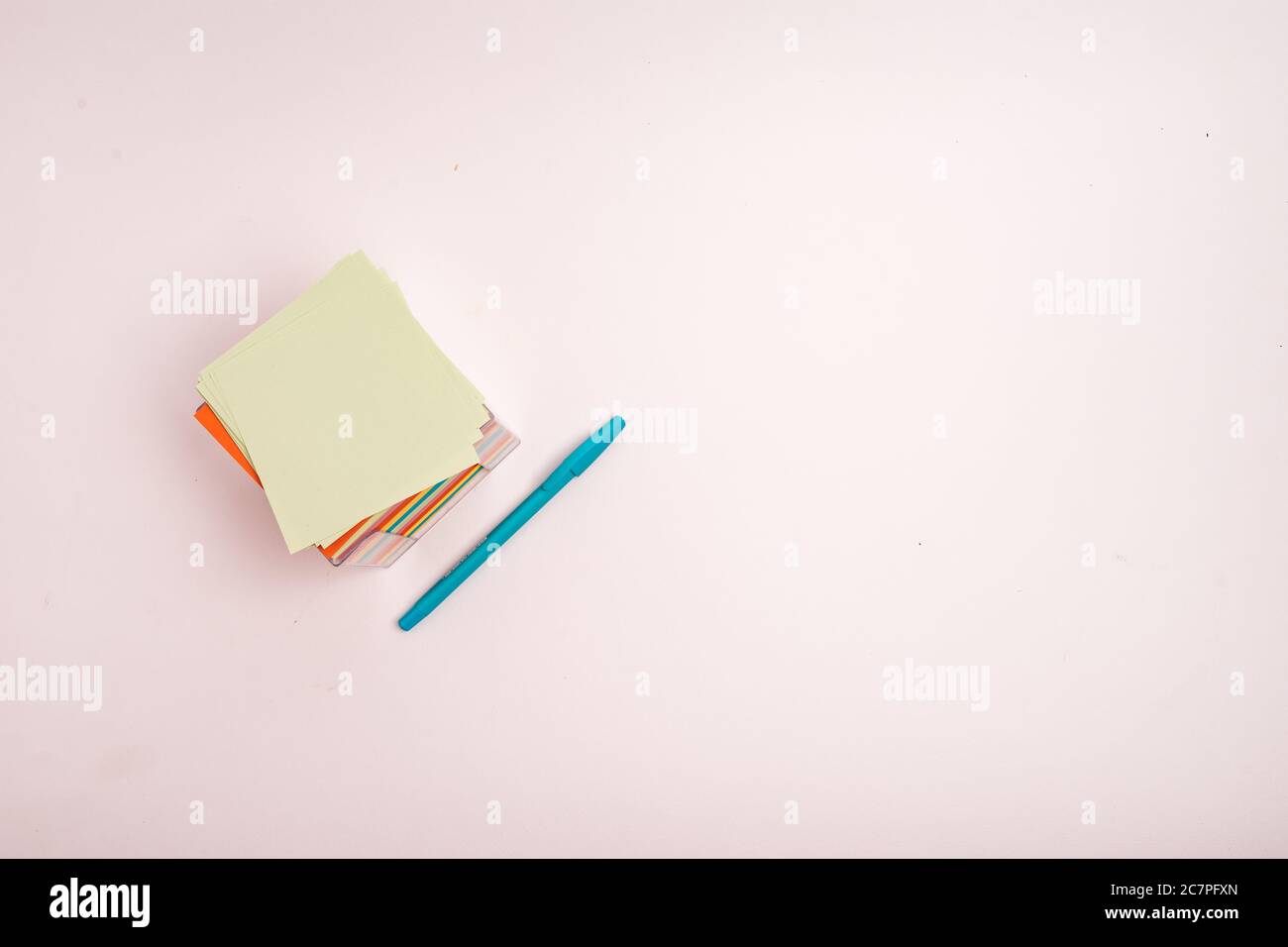 A box with colorful papers and a blue pen isolated on a light-colored background Stock Photo