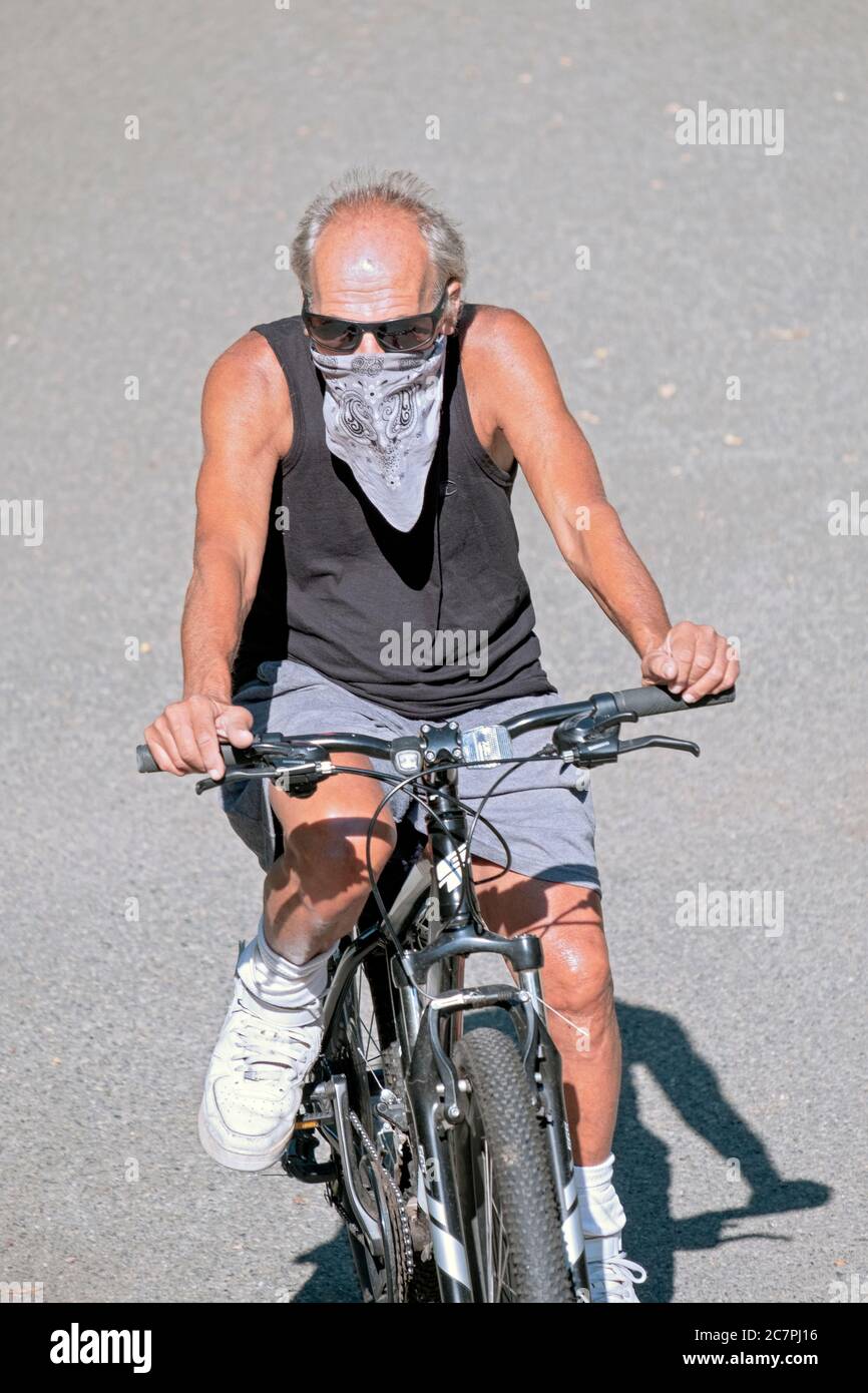 a middle aged man wearing a bandana rides his bike on a path in a park in Flushing, Queens, New York City. Stock Photo