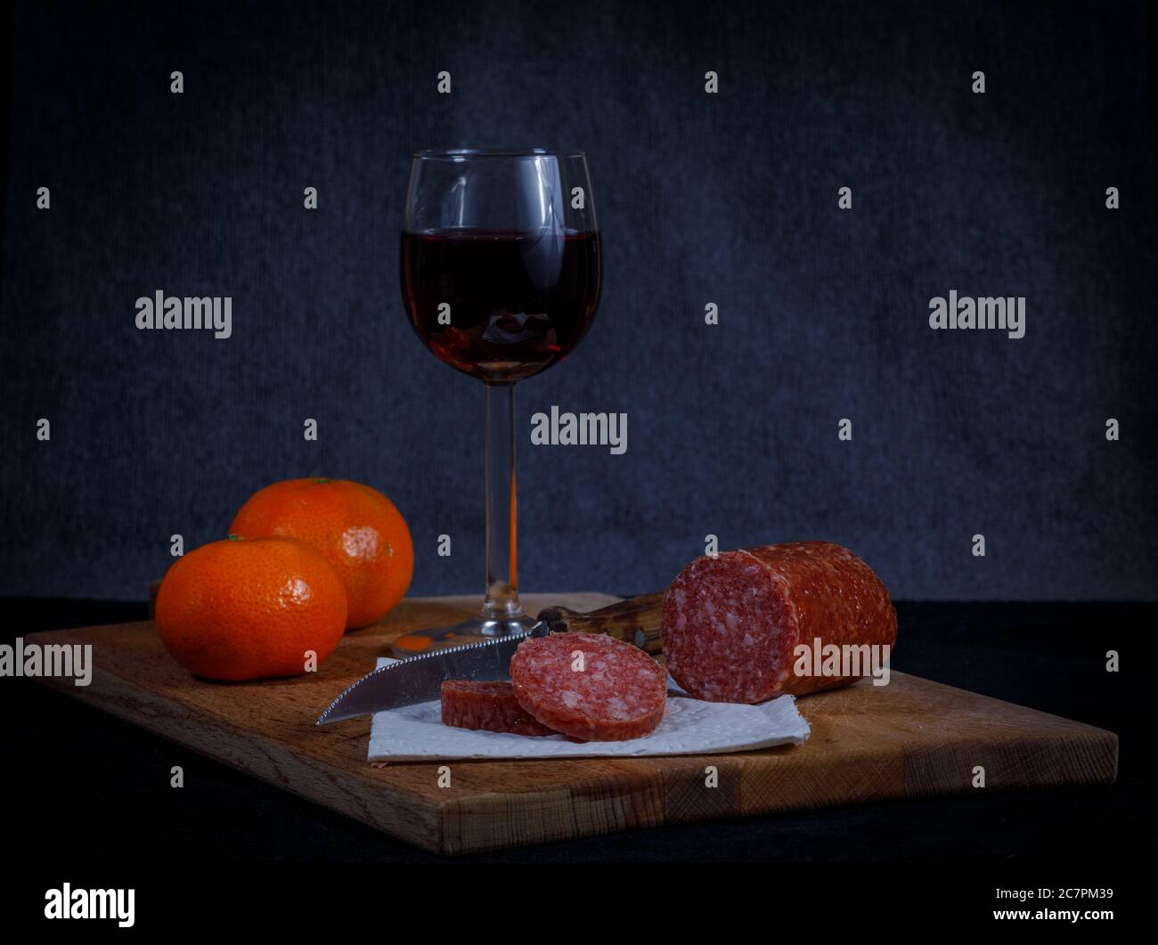 rib gazon zelf Breadboard with a sliced meat saucage, knife and a glas of wine against a  dark background. For color and extra vitamines the mandarins are added  Stock Photo - Alamy