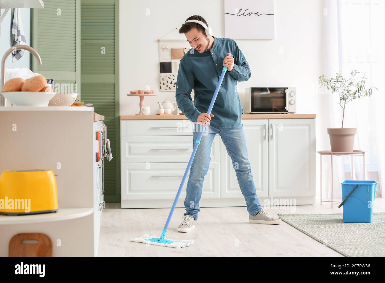 Handsome young man mopping floor in kitchen Stock Photo