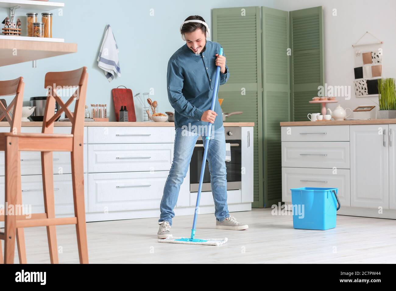 Handsome young man mopping floor in kitchen Stock Photo