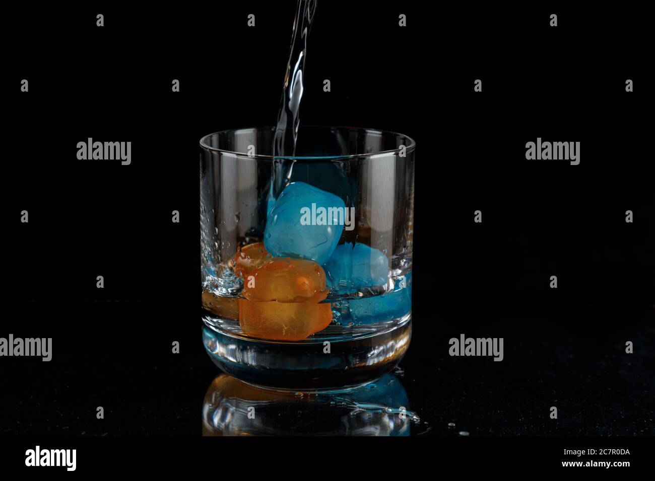 Preparing a drink while pouring over the ice cubes against a black background Stock Photo