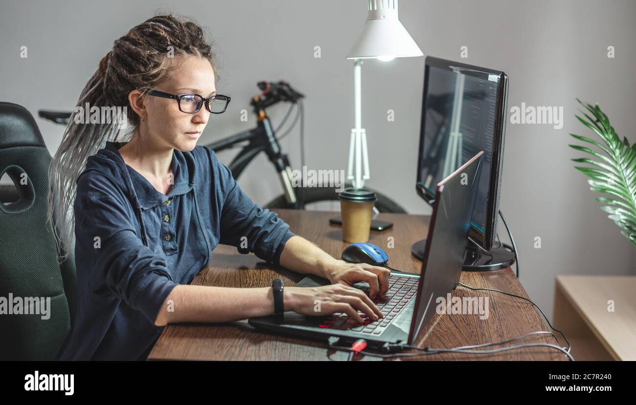 Modern young female programmer is writing program code on a laptop at home. Remote work in the IT profession. The concept of software development. Stock Photo