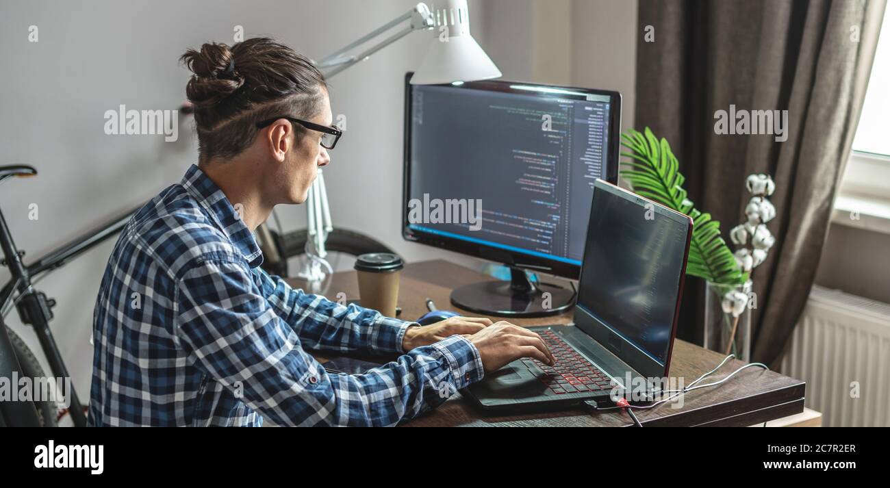Male programmer is writing program code on a laptop at home. Remote work in the IT profession. The concept of software development. Stock Photo