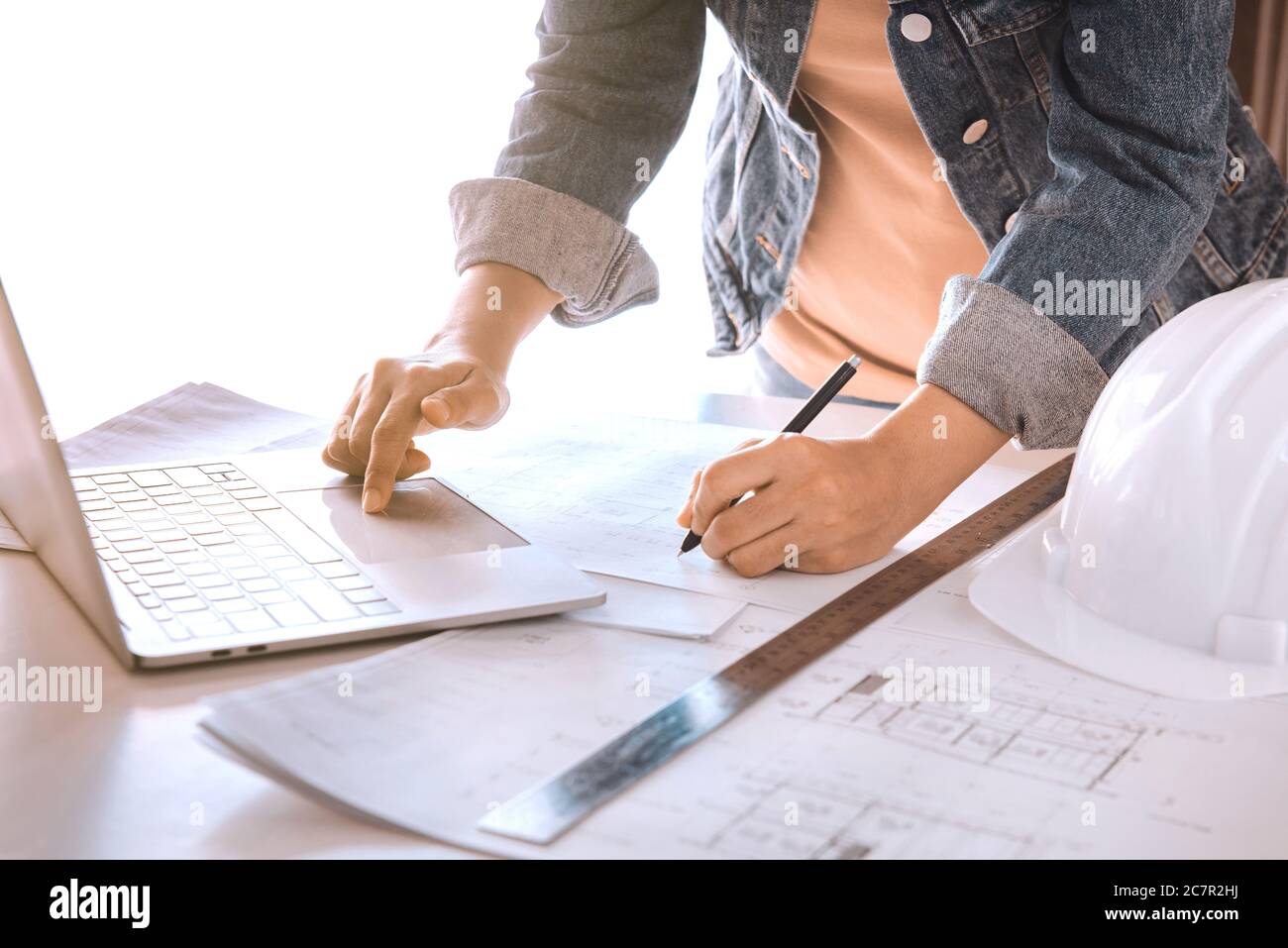 Engineers holding a pen pointing to a building and using laptop to planning project schedule. Engineering and construction concept. Stock Photo