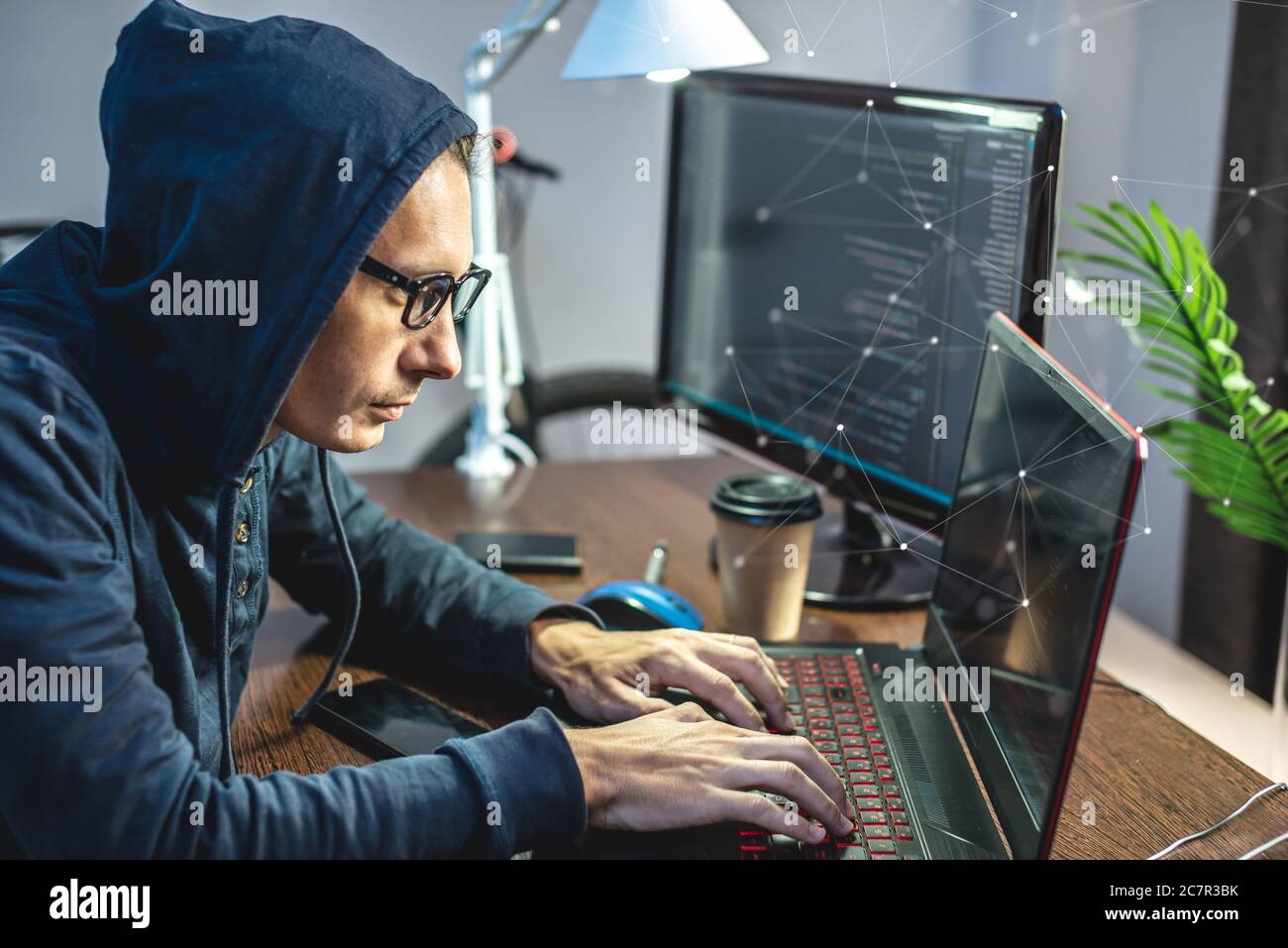 Man hacker in the hood is programming virus code at the keyboard for the laptop. The concept of Internet fraud and personal data hacking Stock Photo