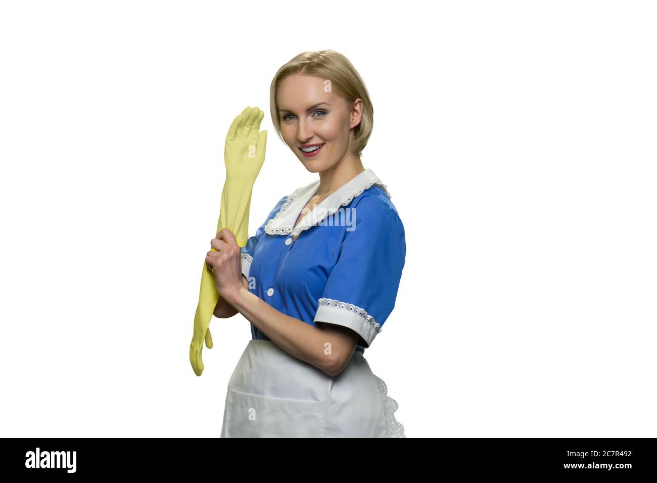 Young blonde maid puts on rubber gloves on white background. Stock Photo