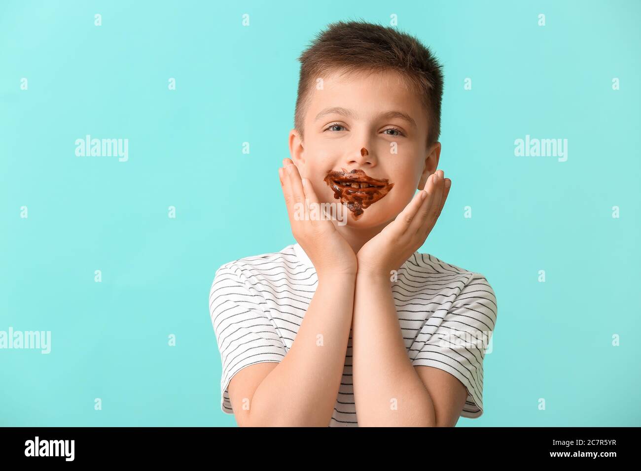 Cute little boy with chocolate on his face against color background