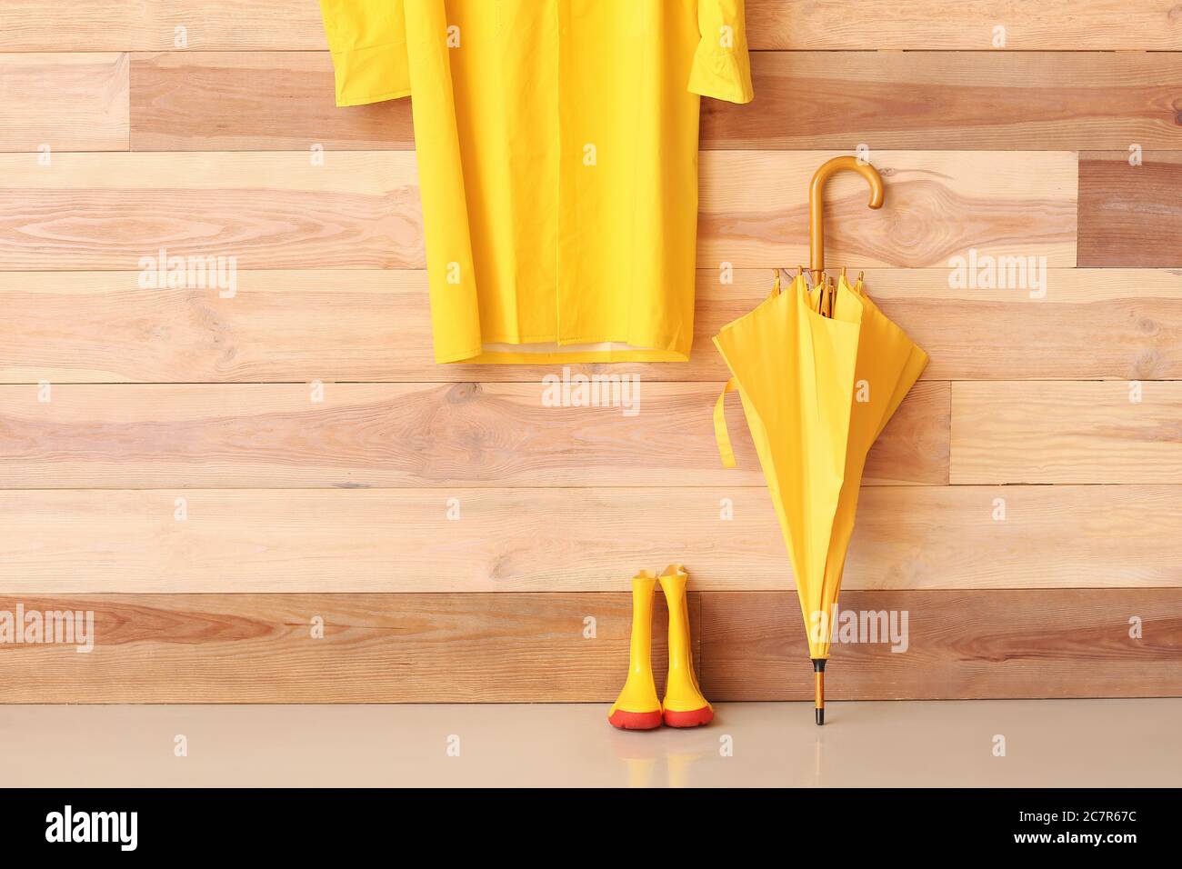 Stylish umbrella, raincoat and gumboots near wooden wall Stock Photo