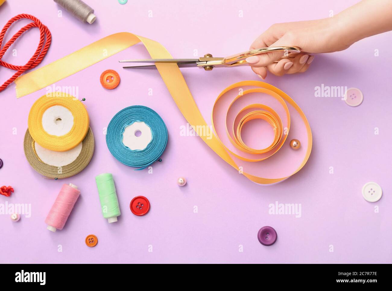Hand of tailor with scissors, ribbons, threads and buttons on color background Stock Photo