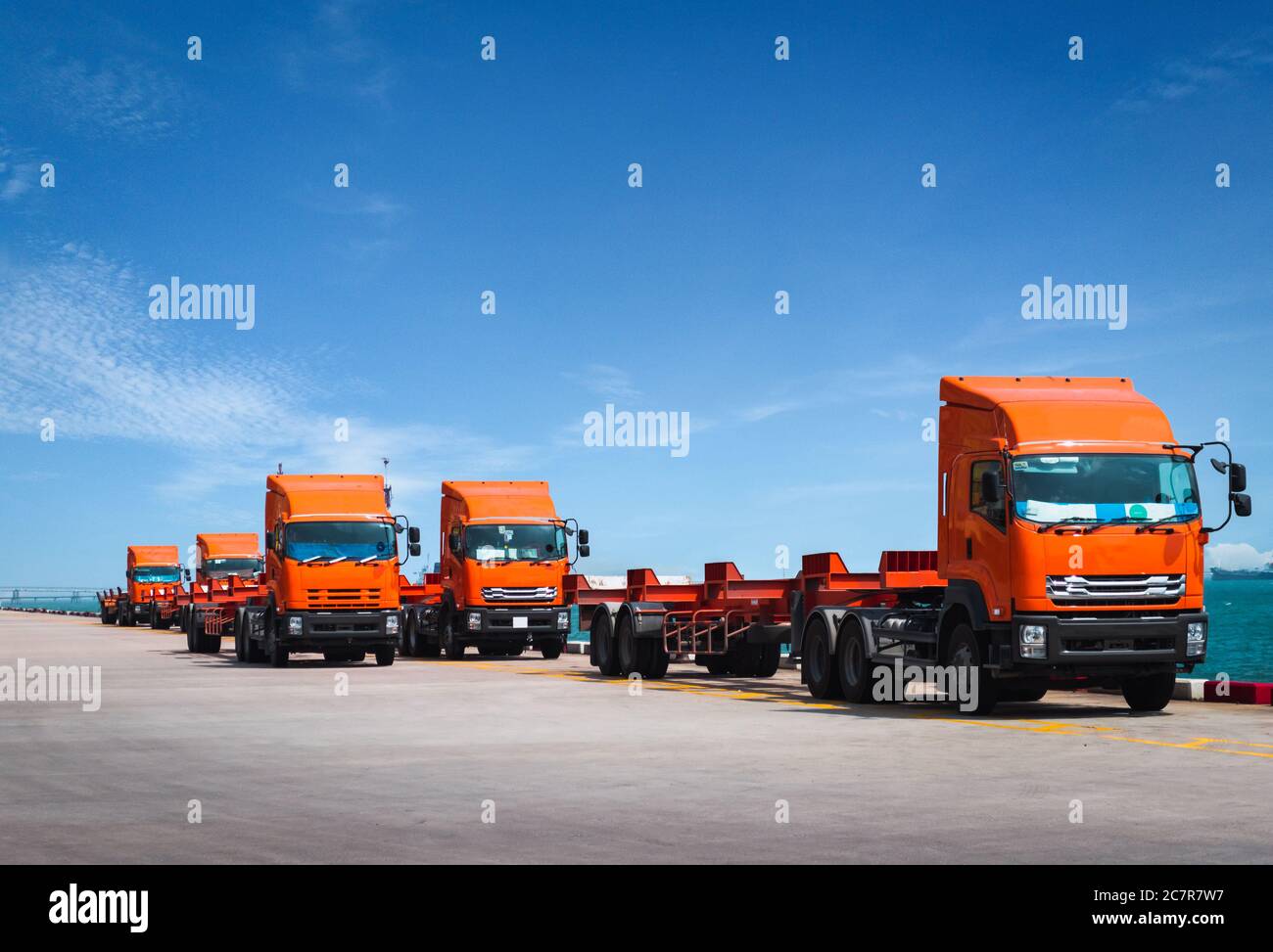 Fleet of trucks and trailer awaiting to pick containers on jetty harbor. Container transportation and logistics, trucking and delivery. Stock Photo