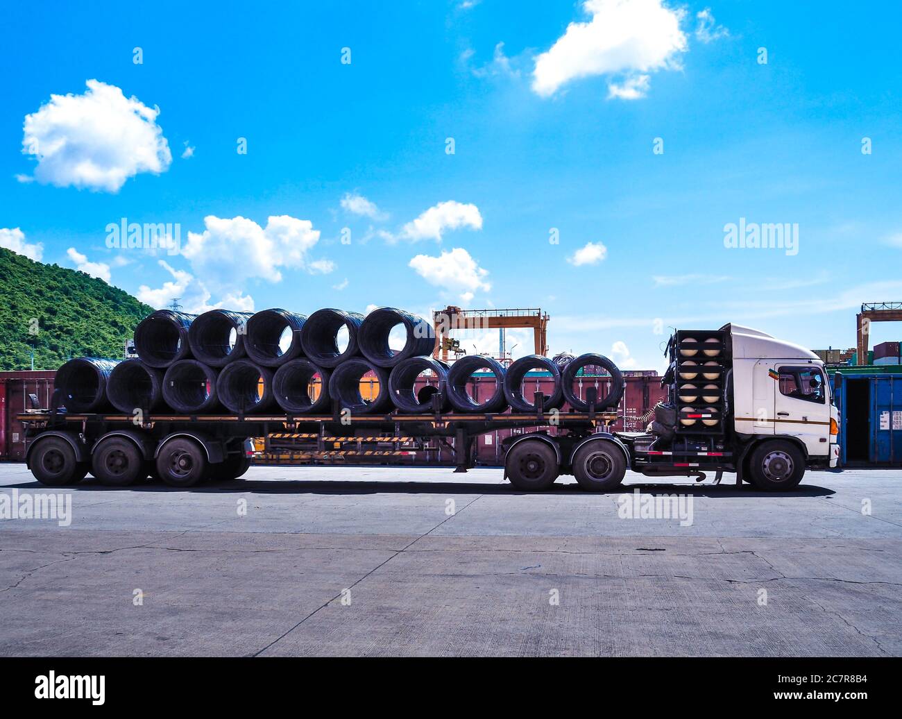 Coils of steel wire rod on truck trailer at industrial zone. Truck receives steel wire rod from warehouse container unstuffing area. Stock Photo