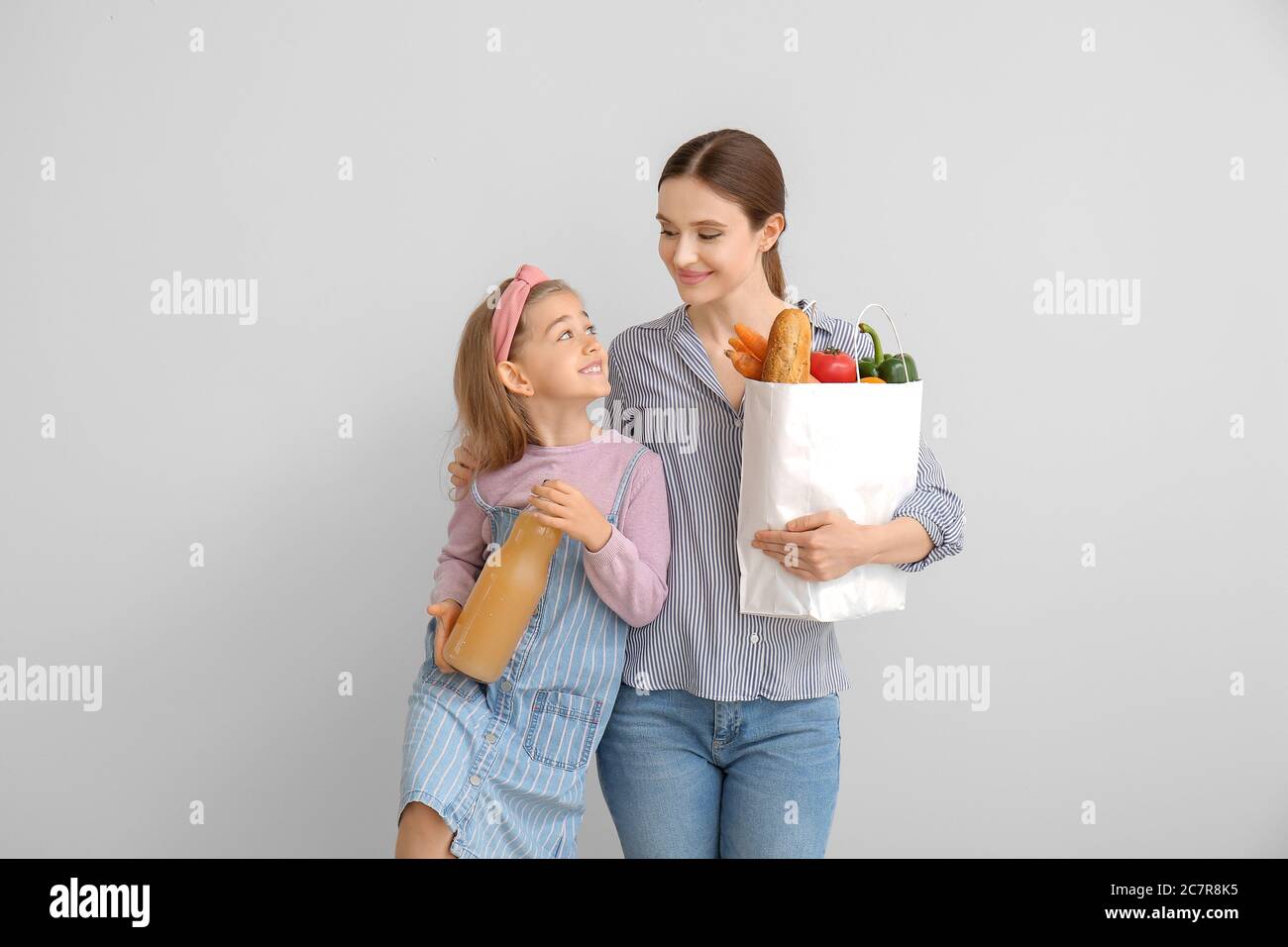Mother and daughter with food in bag on light background Stock Photo