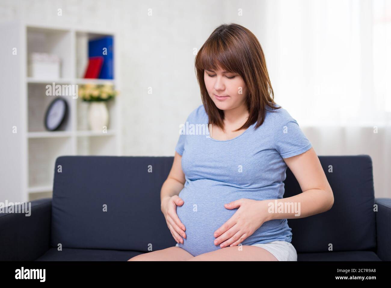portrait of young pregnant woman suffering from abdominal pain at home Stock Photo