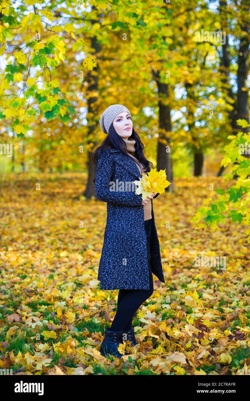 full length portrait of young beautiful woman posing with yellow leaves ...