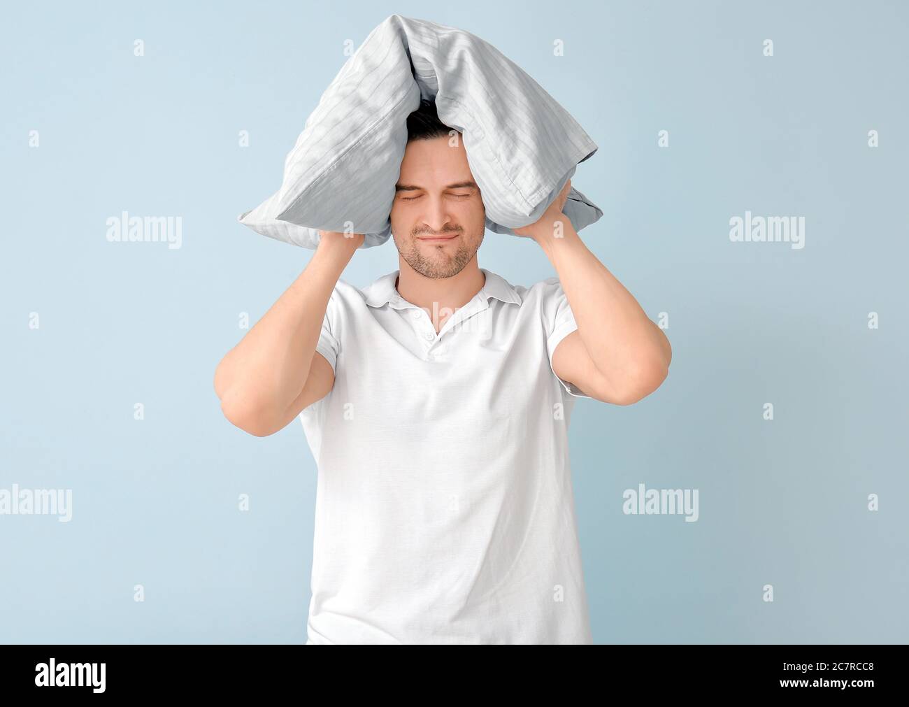 Angry man with pillow on color background. Concept of sleep deprivation Stock Photo