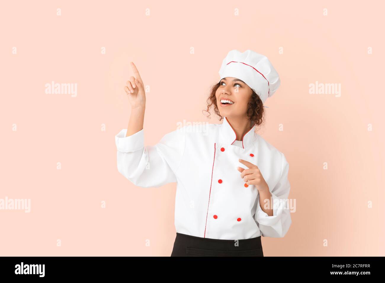 Female African-American chef pointing at something on color background Stock Photo